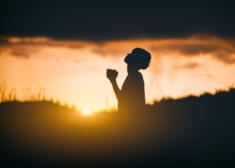 Young christian sitting and pray to God at sunset background. ch